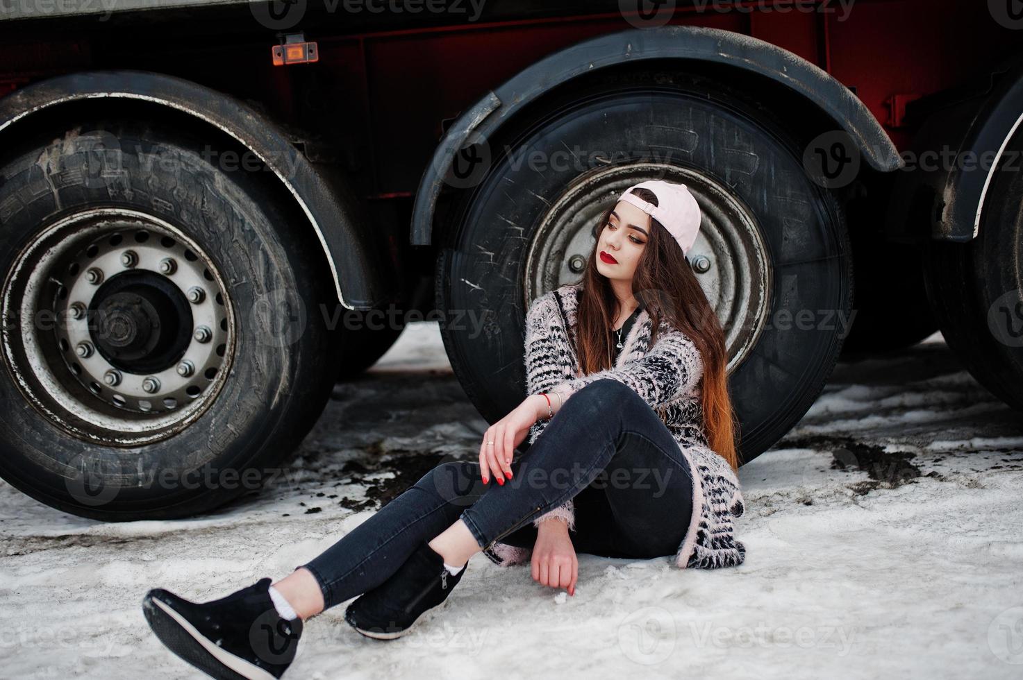 brunett snygg casual flicka i mössa sitter mot lastbil hjul. foto