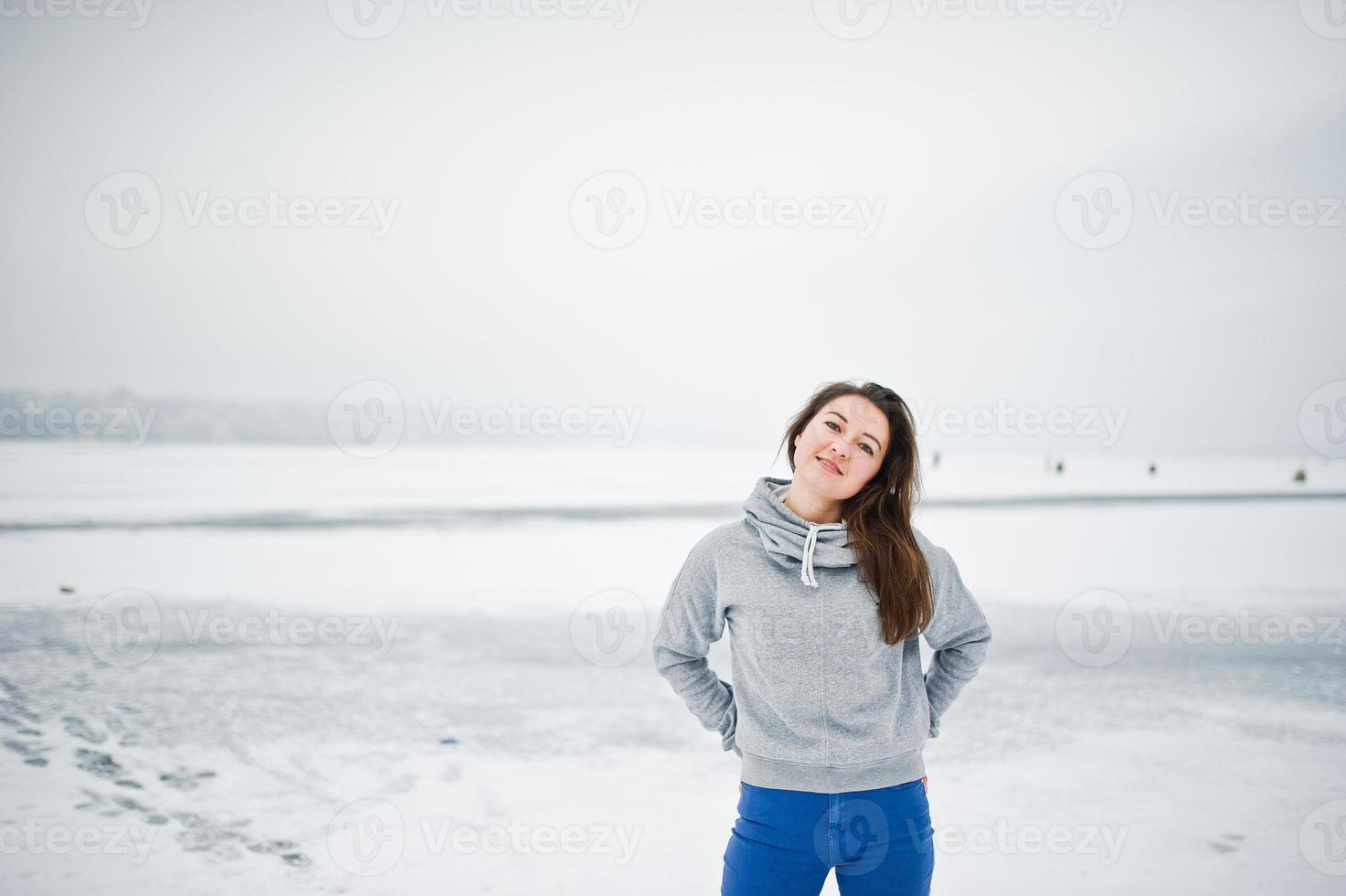 rolig tjej slitage på hoody tröja och jeans, vid frusen sjö i vinterdag. foto