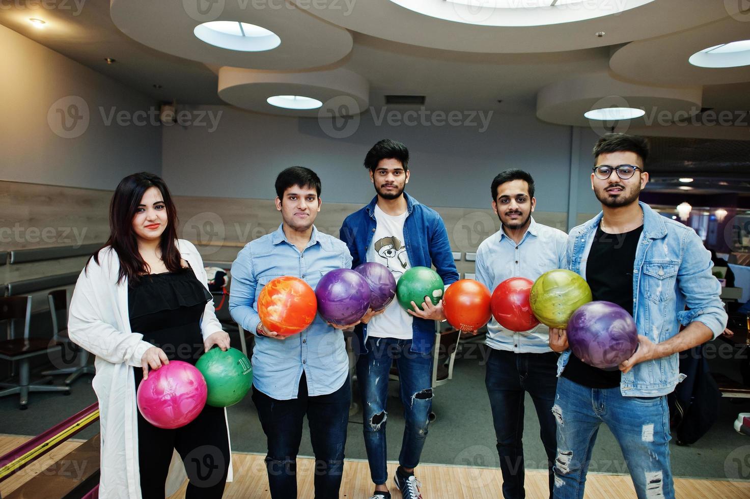 grupp av fem sydasiatiska folk som har vila och roligt på bowlingklubben. håller bowlingklot i händerna. foto