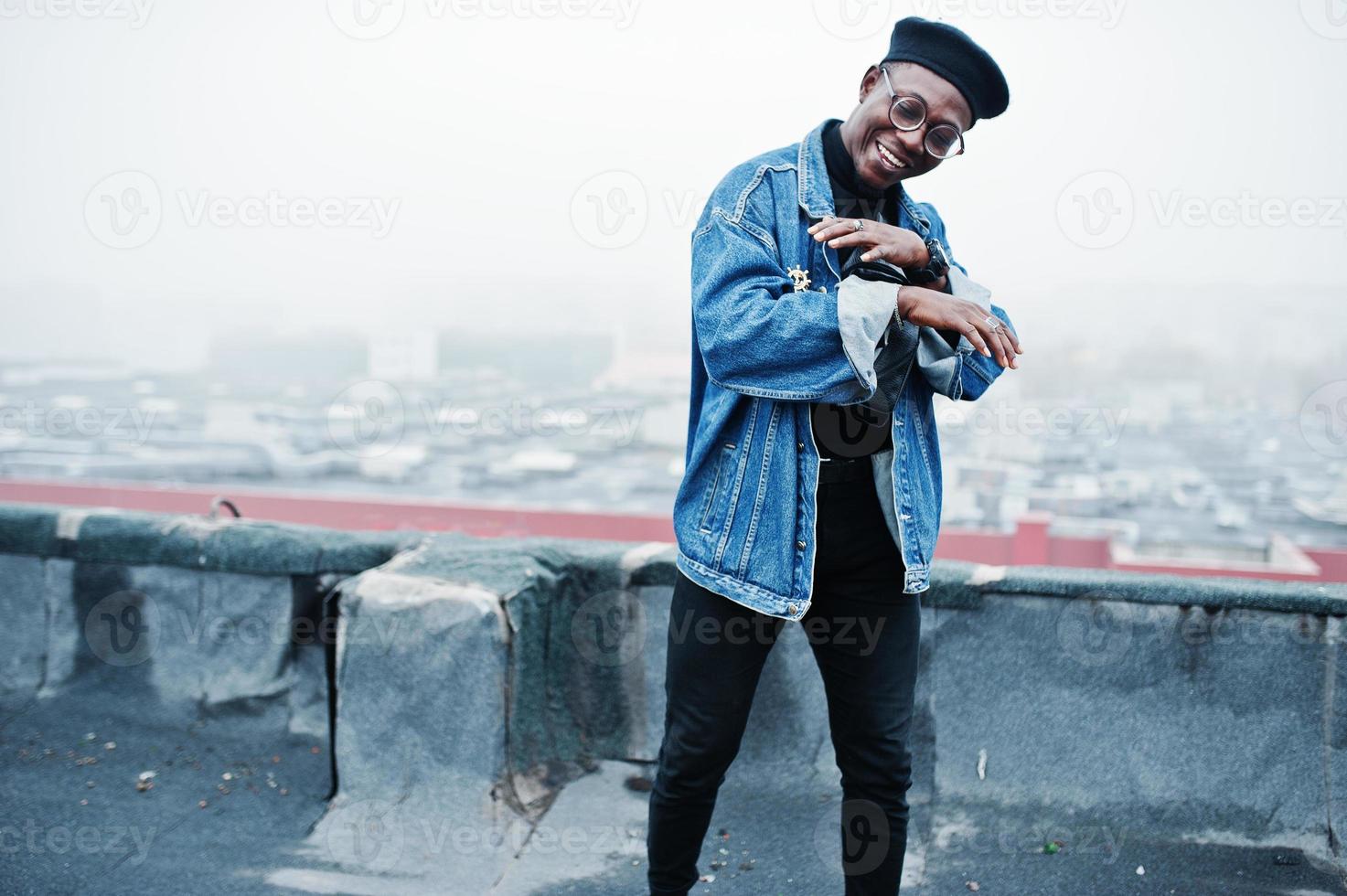 afroamerikansk man i jeansjacka, basker och glasögon poserade på övergivet tak. foto