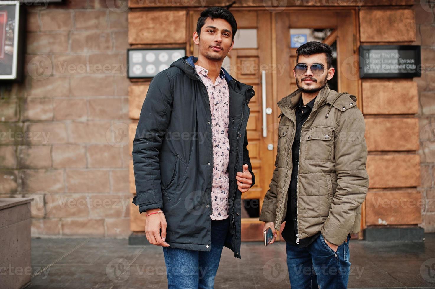två indiska killar på jackor poserade utomhus mot dörren till puben. foto