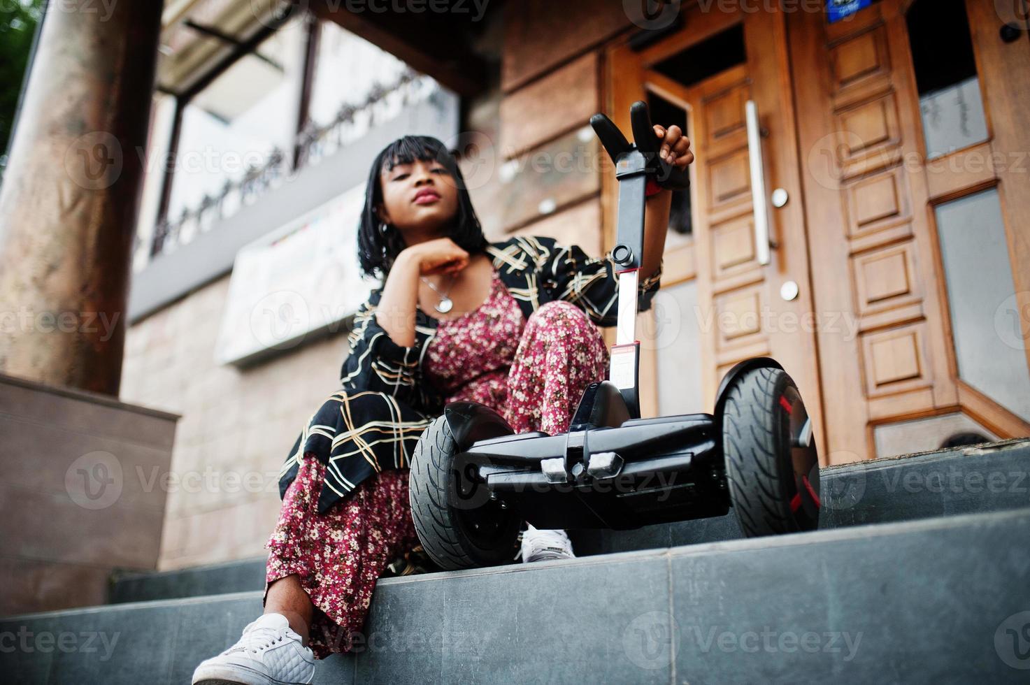 vacker afrikansk amerikansk kvinna sitter nära segway eller hoverboard. svart flicka med dubbla hjul självbalanserande elektrisk skoter. foto