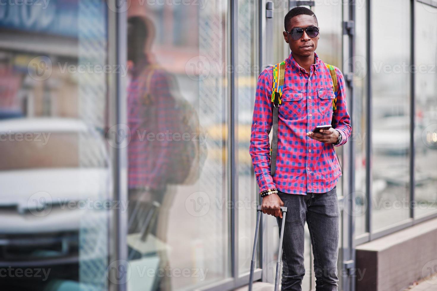 afrikansk amerikansk man i rutig skjorta, med resväska och ryggsäck. svart man resenär mot busstationen. foto
