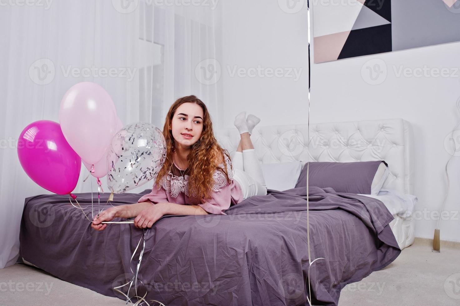 ung flicka med ballonger på sängen poserade på studio rum. foto