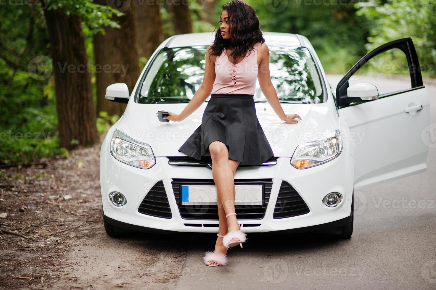 afrikansk amerikansk kvinna poserade mot vit bil i skogsväg. foto