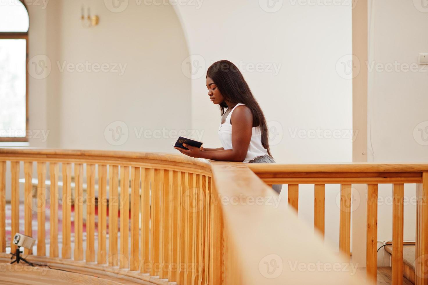 afrikansk amerikansk kvinna ber i kyrkan. troende mediterar i katedralen och andlig bönetid. afro flicka med Bibeln i händerna. foto