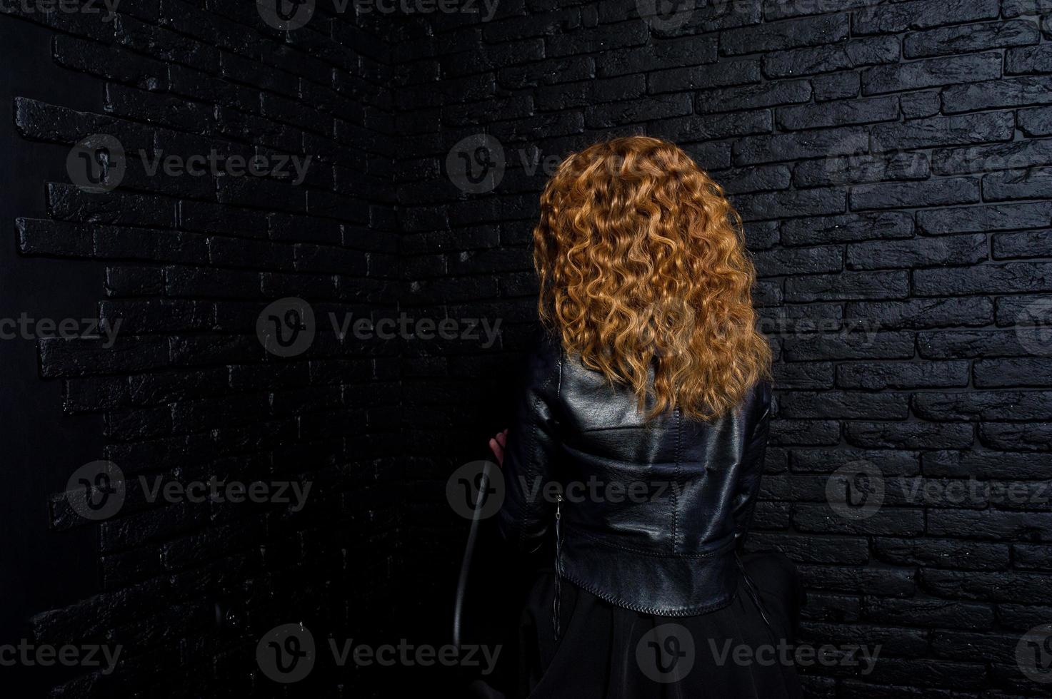 lockigt hår flicka på skinnjacka på studio mot svart tegelvägg. foto