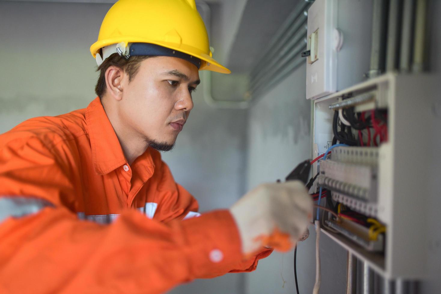 sidovy av en stilig asiatisk elektriker som reparerar en ellåda med tång i korridoren. foto