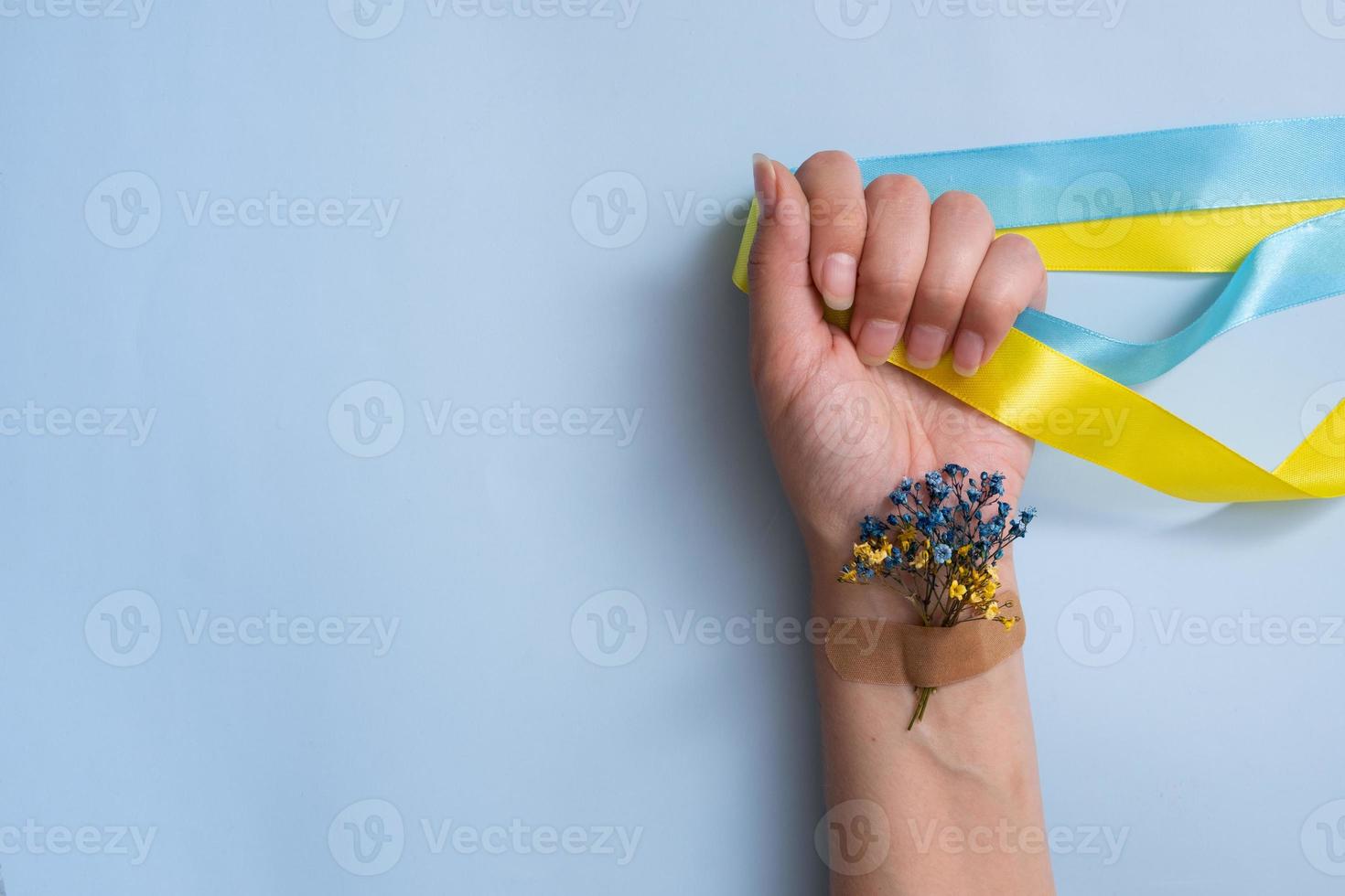 kvinnlig hand med gula och blå band och blommor på en blå bakgrund. älska och be till Ukraina koncept foto