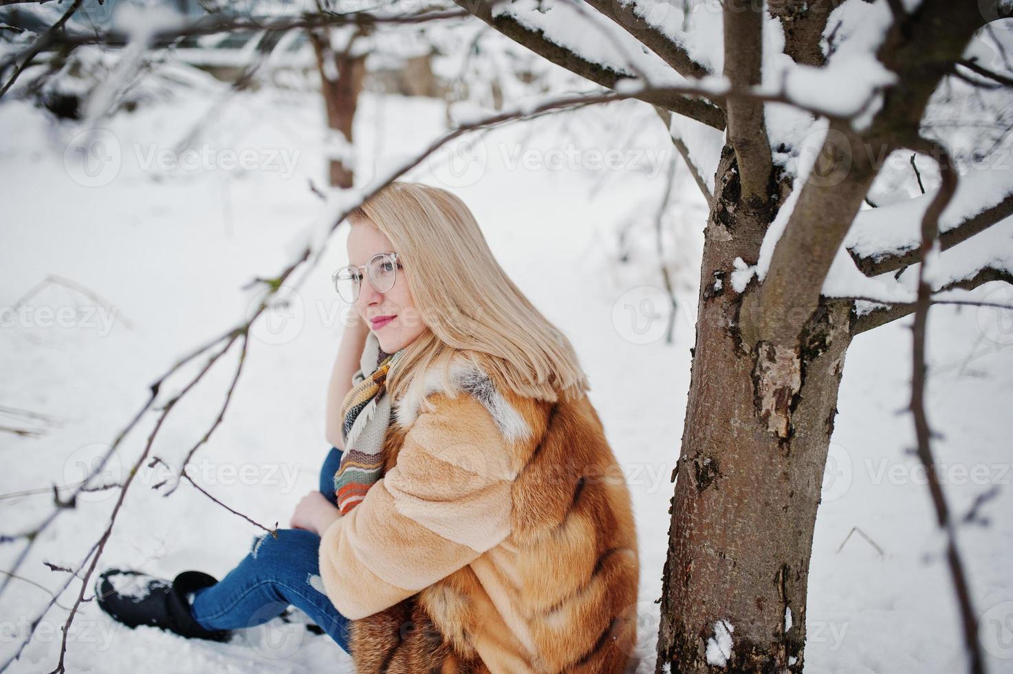 porträtt av blond flicka i glasögon, röd päls och halsduk på vinterdagen. foto