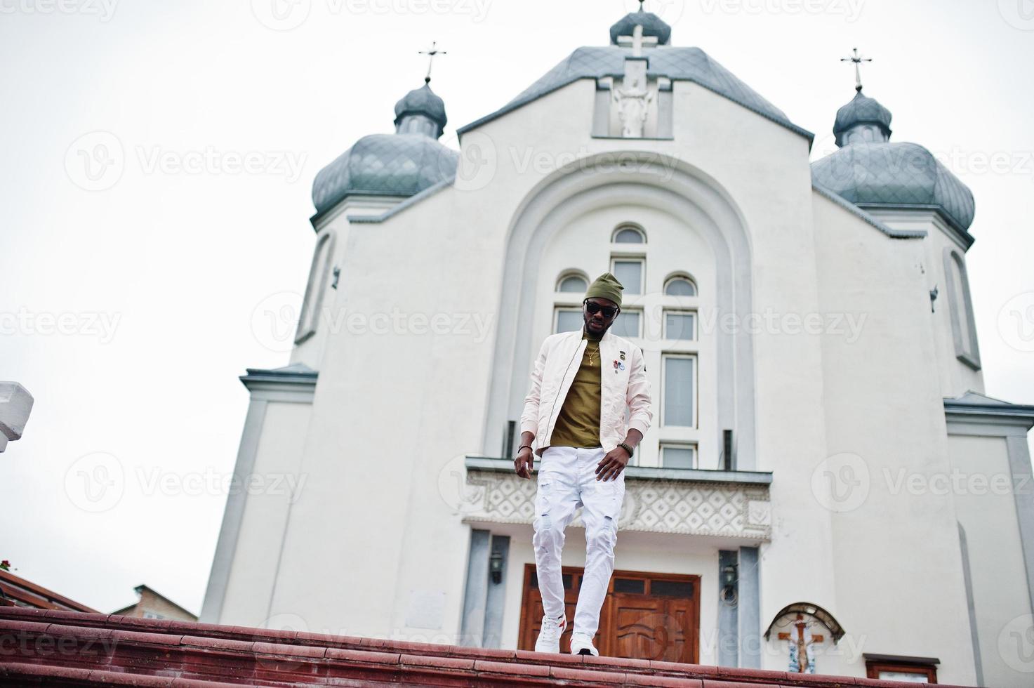 afrikansk amerikansk man i hatt och solglasögon står mot kyrkan. tro och kristendom i afrika. foto