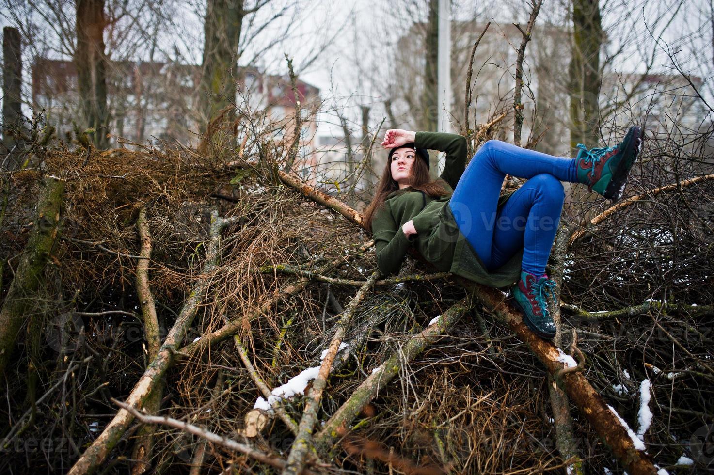 ung flicka bär på lång grön tröja, jeans och svarta huvudbonader vid grenar av tallen i vinterdag. foto