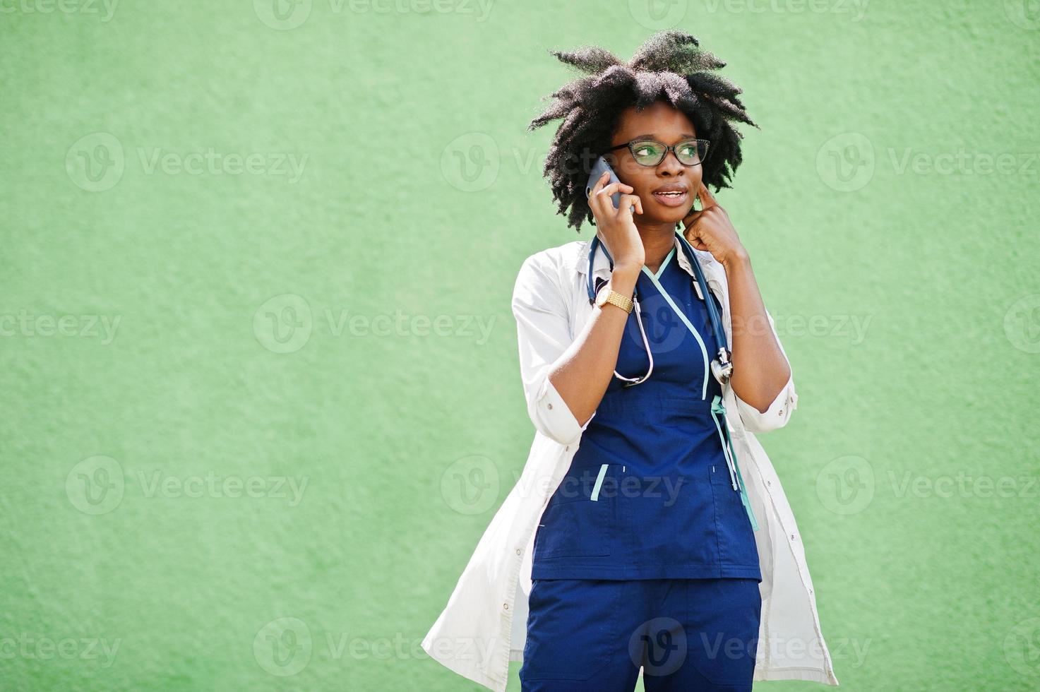 porträtt av afrikansk amerikansk kvinnlig läkare med stetoskop bär labbrock, talar med mobiltelefon. foto