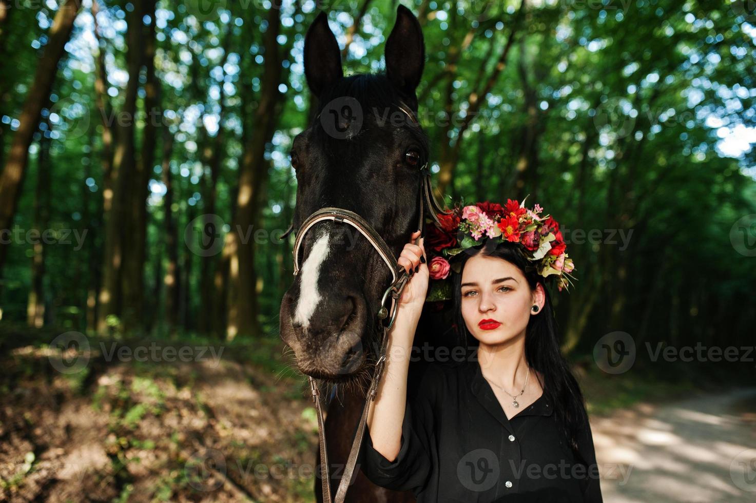 mystisk flicka i krans slitage i svart med häst i trä. foto