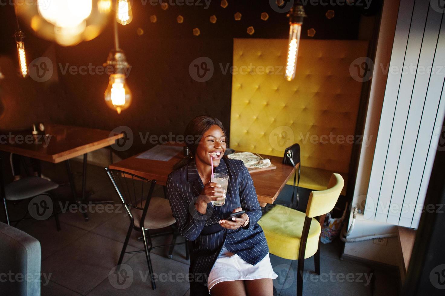 afrikansk amerikansk affärskvinna dricker cocktail lemonad i café. svart flicka med vila med mobiltelefon. foto