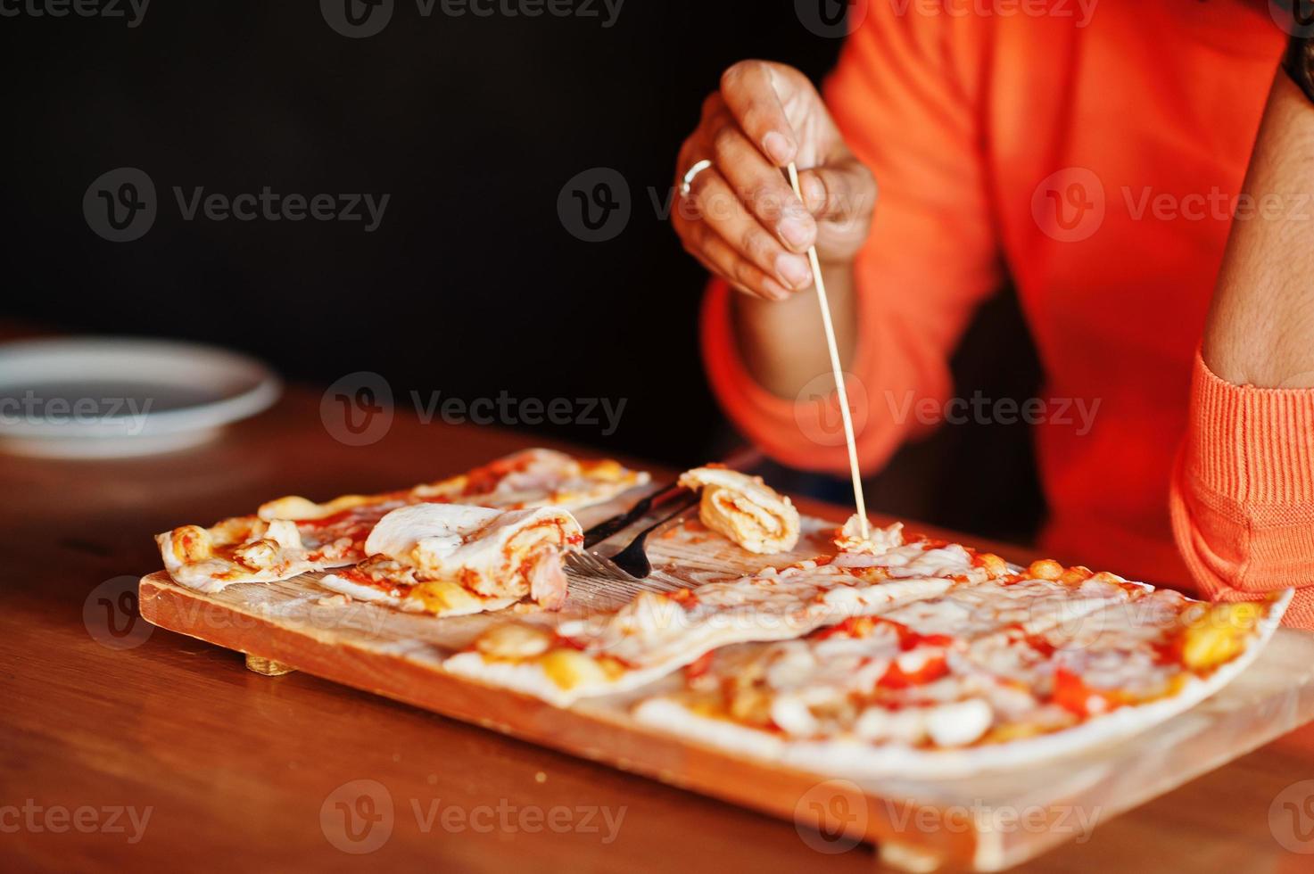 närbild hand av mannen i orange tröja sitter på pizzeria med pizza. foto