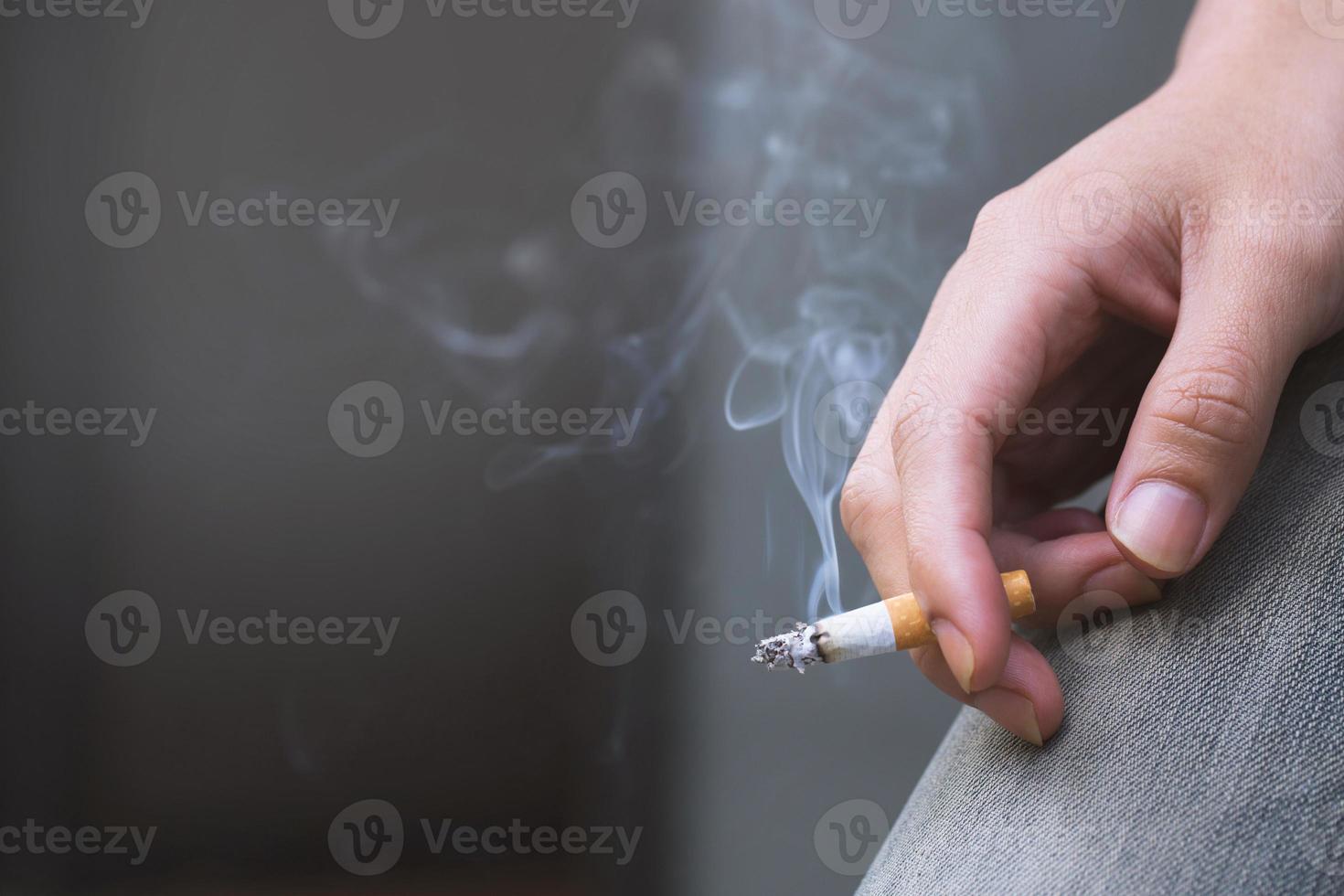 man håller röka en cigarett i handen. cigarettrök spred sig. mörk bakgrund foto