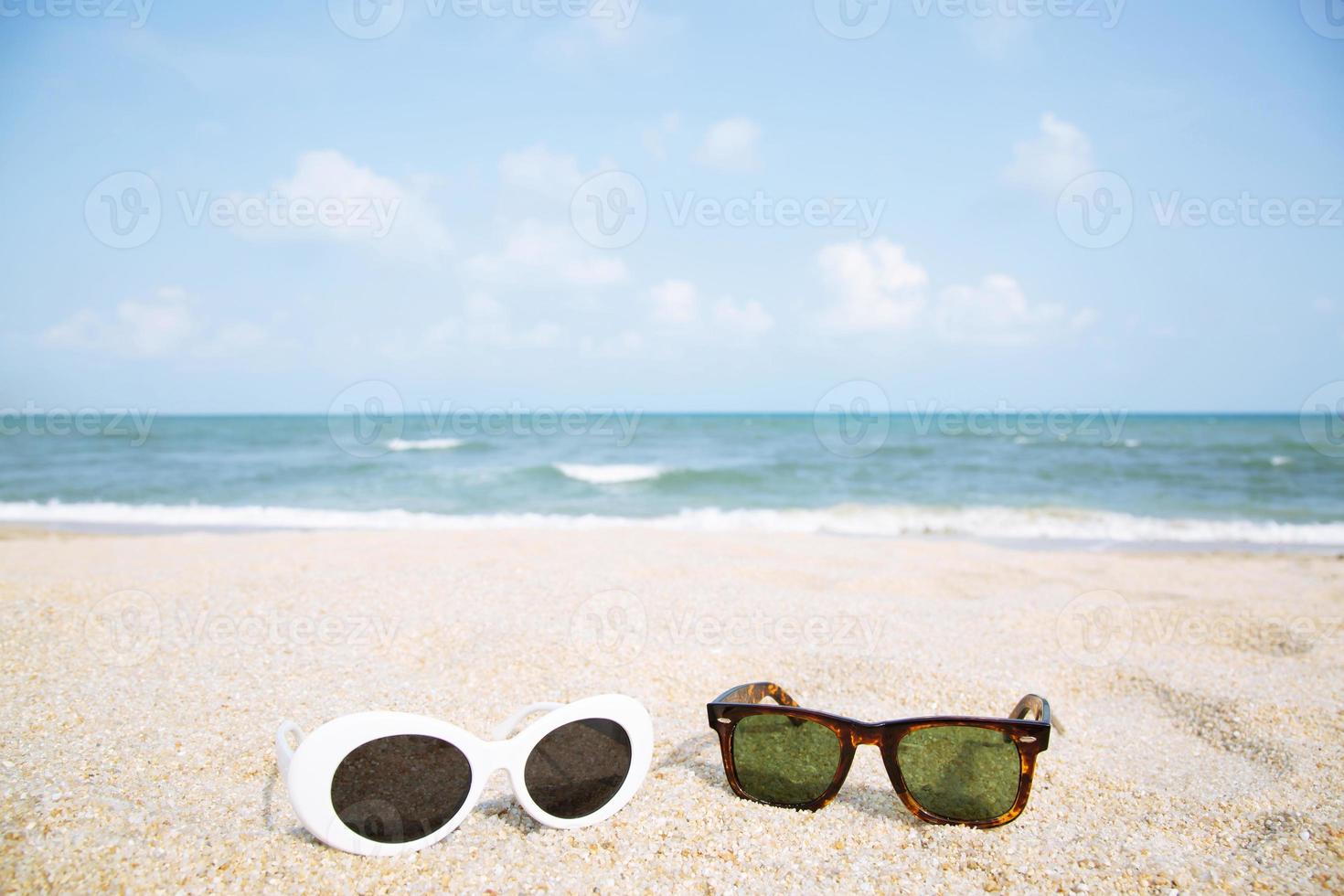 två mode solglasögon närbild på strandsanden på sommaren. vacker havsutsikt klarblå himmel tapeter, sommarsemester slappna av bakgrund med kopia utrymme. solglasögon resor par älskare koncept. foto