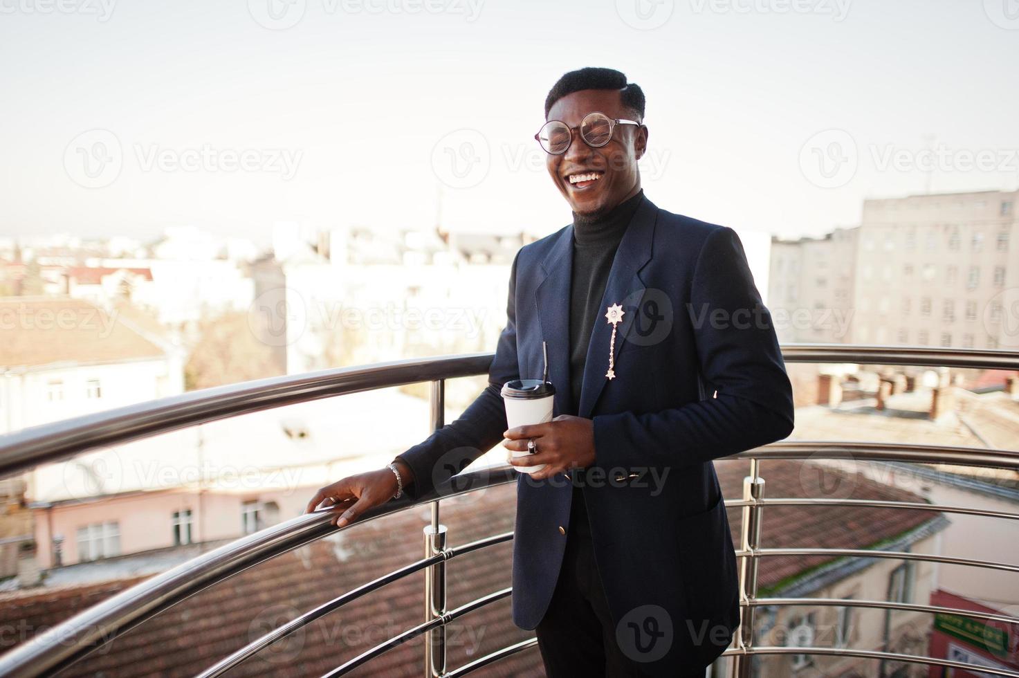 fashionabla afrikansk amerikansk man i kostym och glasögon med en kopp kaffe vid händerna poserade på balkongen på kontoret. foto