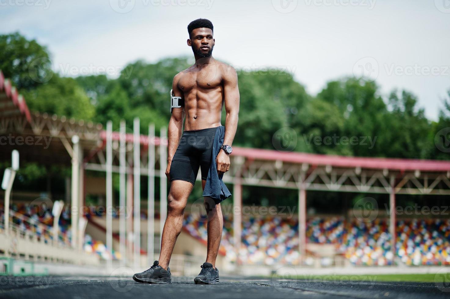 afrikansk amerikansk manlig idrottare sexig sport bar överkropp man med löpande sportarmfodral för mobiltelefon, poserade på stadion. foto