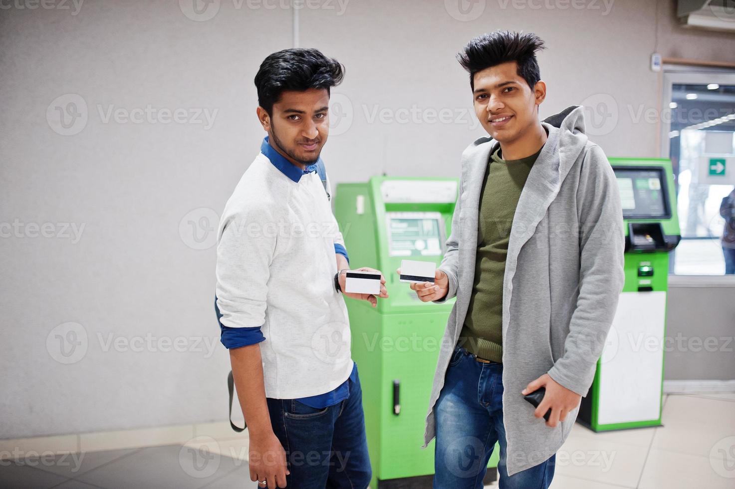 två asiatiska killar som håller kreditkort i handen mot grön bankomat. foto