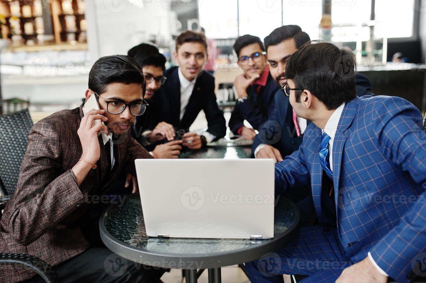 grupp av sex indisk affärsman i kostym sitter på kontoret på café och tittar på laptop. foto