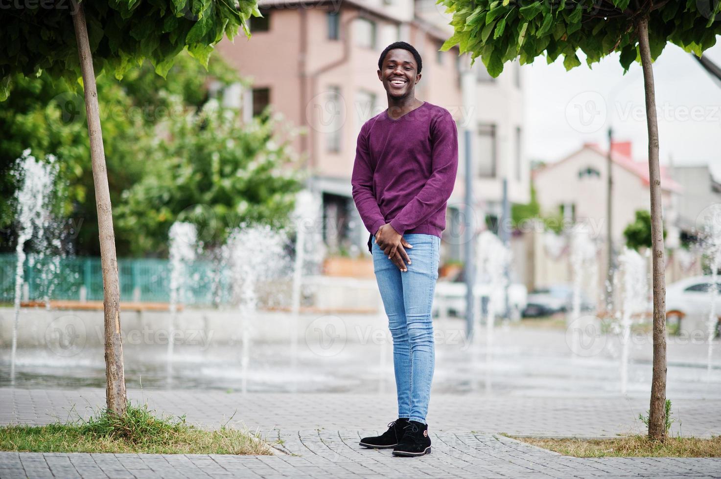 ung afroamerikansk man i violett tröja poserade mot fontän gränd. foto