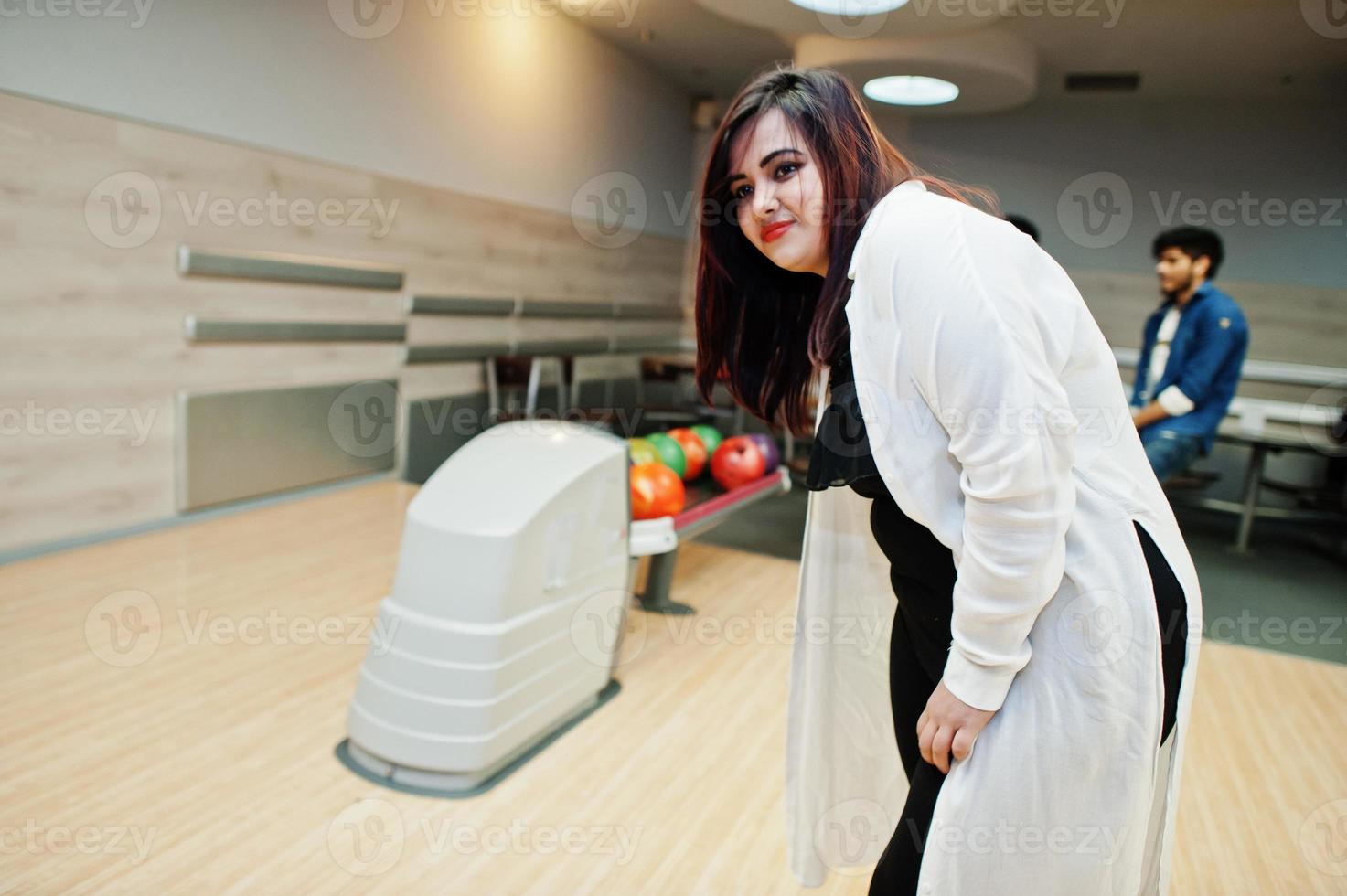 sydasiatisk kvinna står vid bowlinghall med boll på händerna. flickan förbereder sig för ett kast. foto