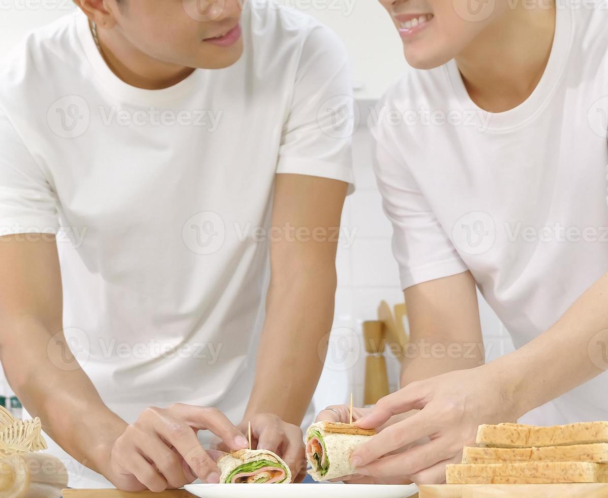 två rull smörgås sätta på tallriken med manliga par händer, glada leende ansikte i köket tillsammans. Hbt hemlivskoncept. vertikalt beskuren bild. selektiv fokusering. foto
