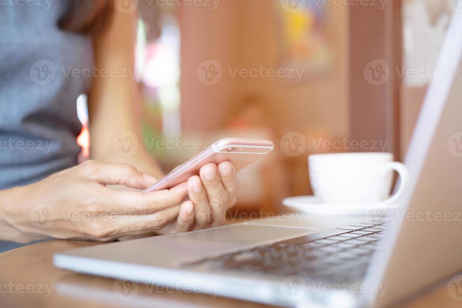 närbild hand människor person kvinna vid dator bärbar dator med mobiltelefon sitta på trägolv. lämna utrymme för text på skärmen koncept. foto