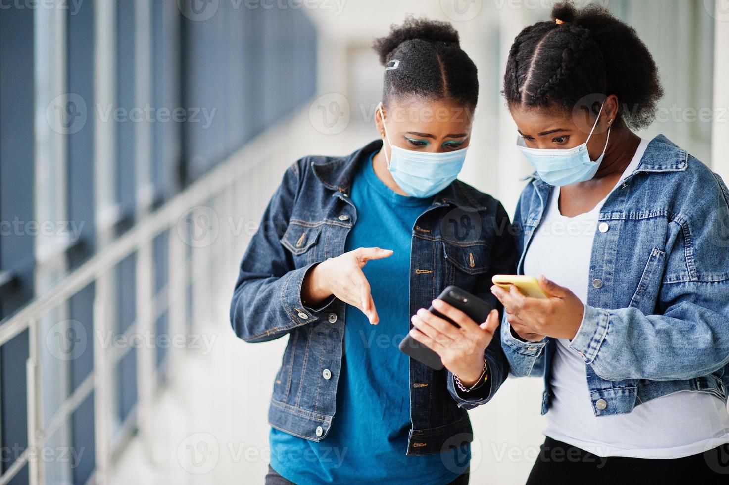 två afrikansk kvinna vänner i jeansjacka bär skyddsmasker med mobiltelefoner. virus koncept hälsa, medicinsk. foto