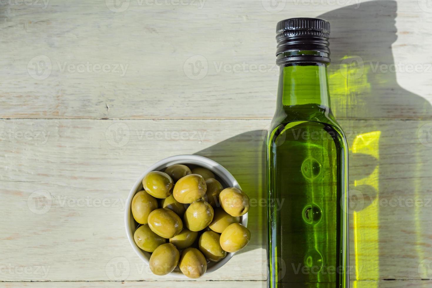 extra virgin olivolja i grön flaska och färska gröna oliver på träbord. foto