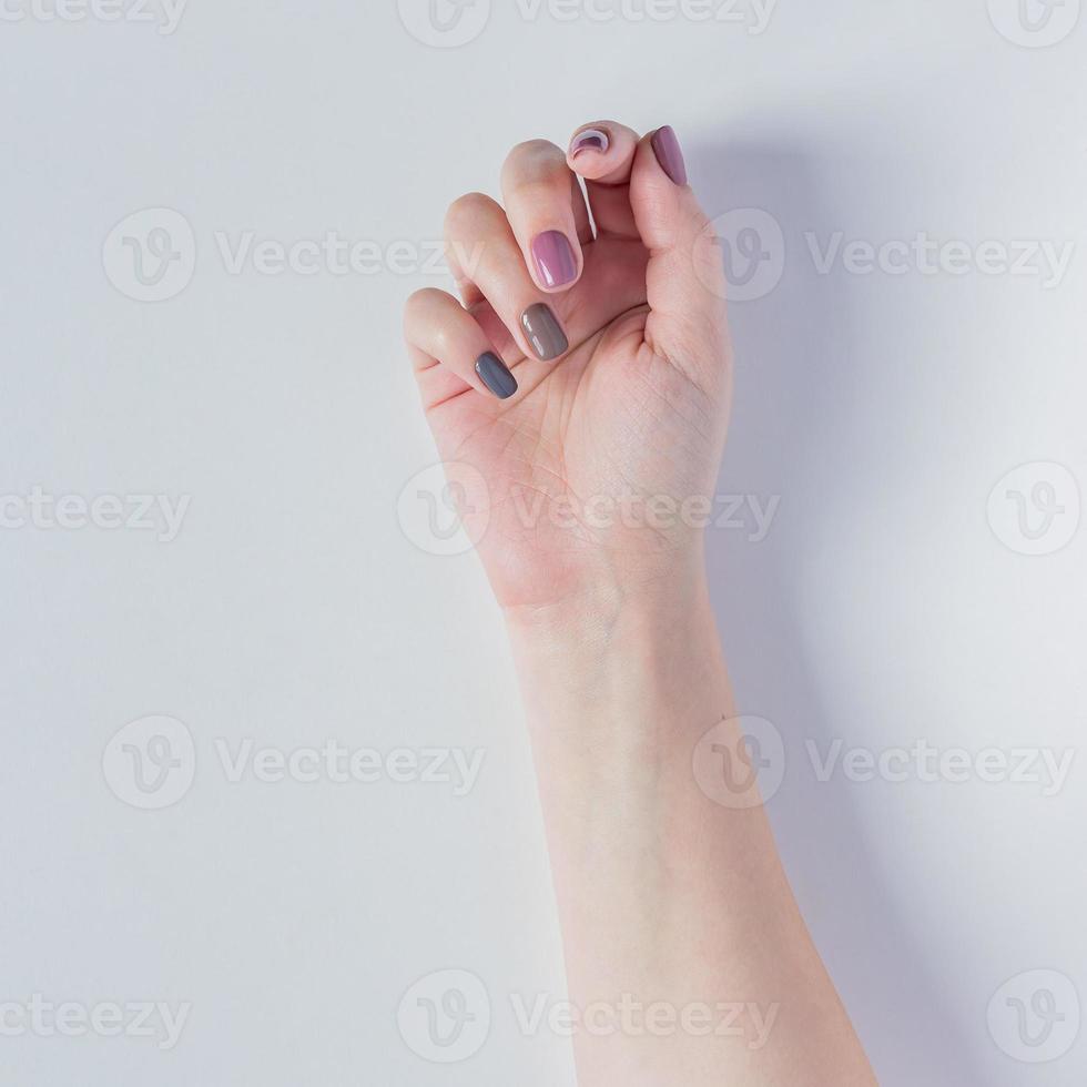 vacker ung kvinnas hand på vit bakgrund. snygg trendig kvinnlig manikyr med grått, rosa och brunt nagellack. naturliga naglar foto