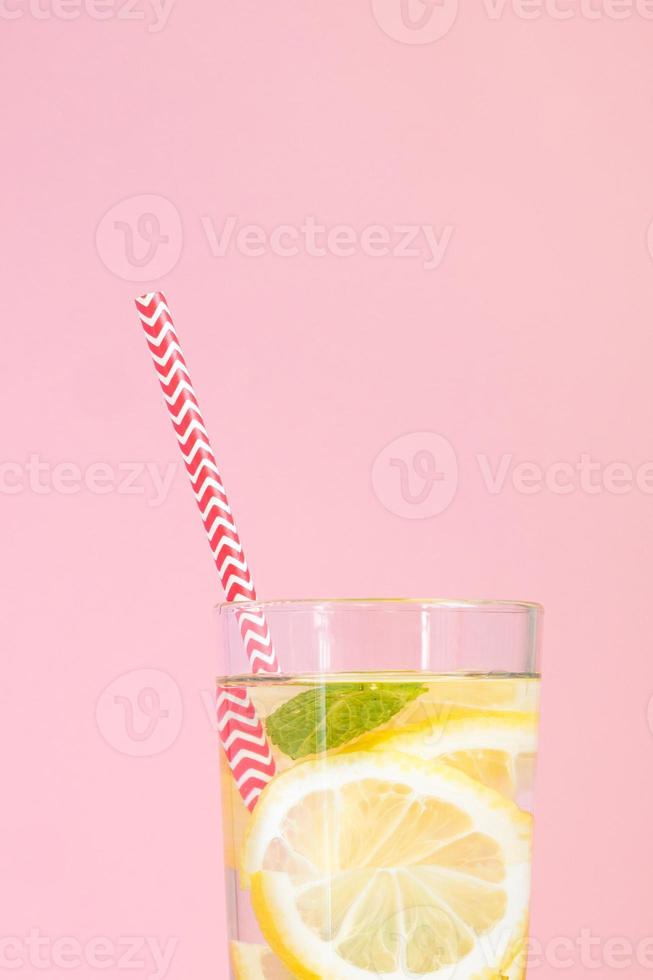 glas hemlagad lemonad med citroner, mynta och rött pappersstrå på rosa bakgrund. sommarens uppfriskande dryck. foto