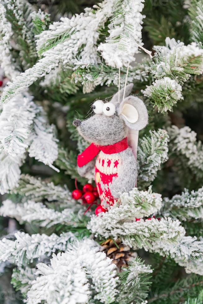 symbol för året 2020. vit leksaksråtta i julhatt hängande på päls snöigt träd. festlig inredning. foto