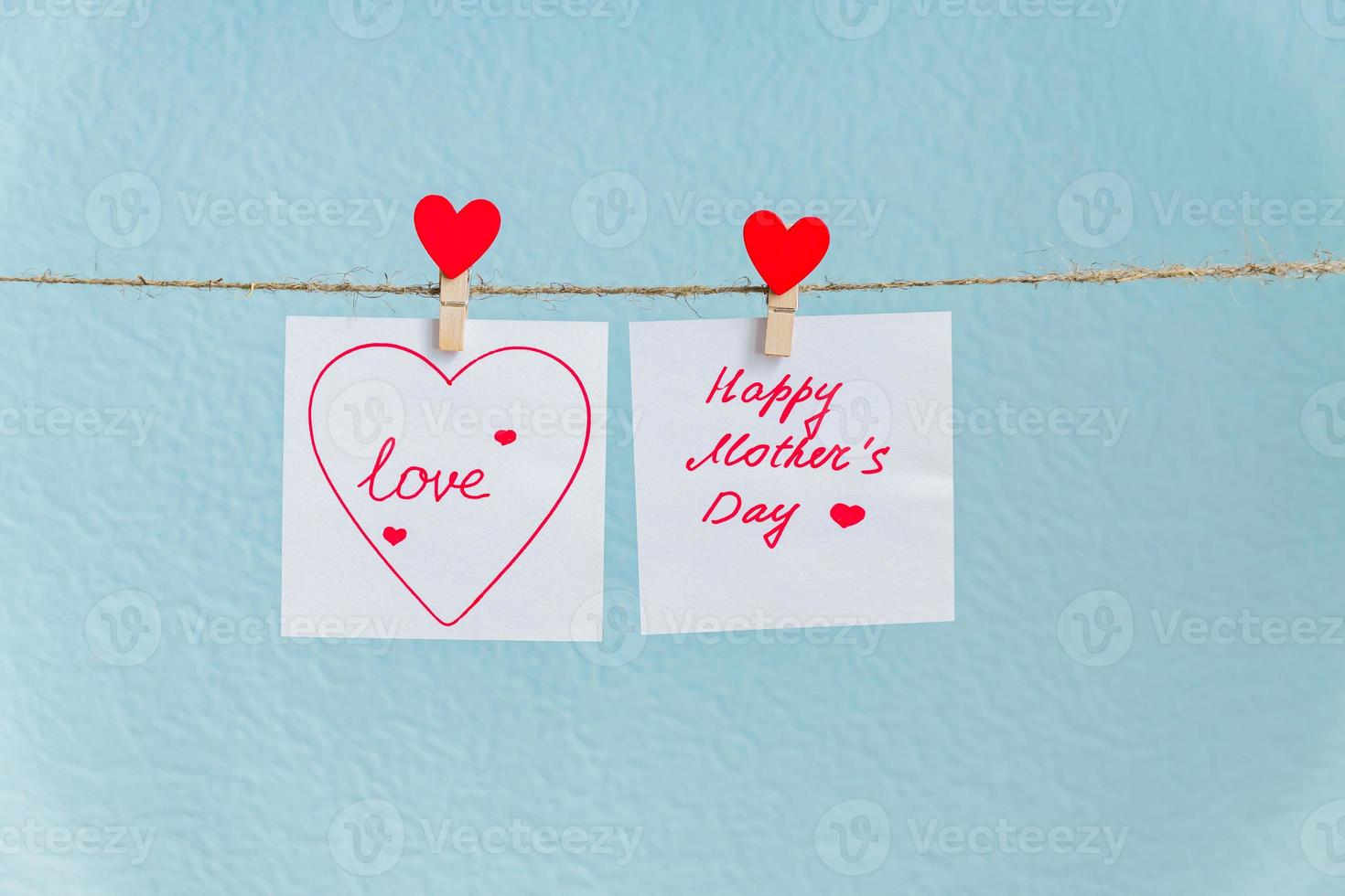 röda kärlekshjärtan stift hängande på naturlig sladd mot blå bakgrund. glad mors dag inskription på pappersbit. foto
