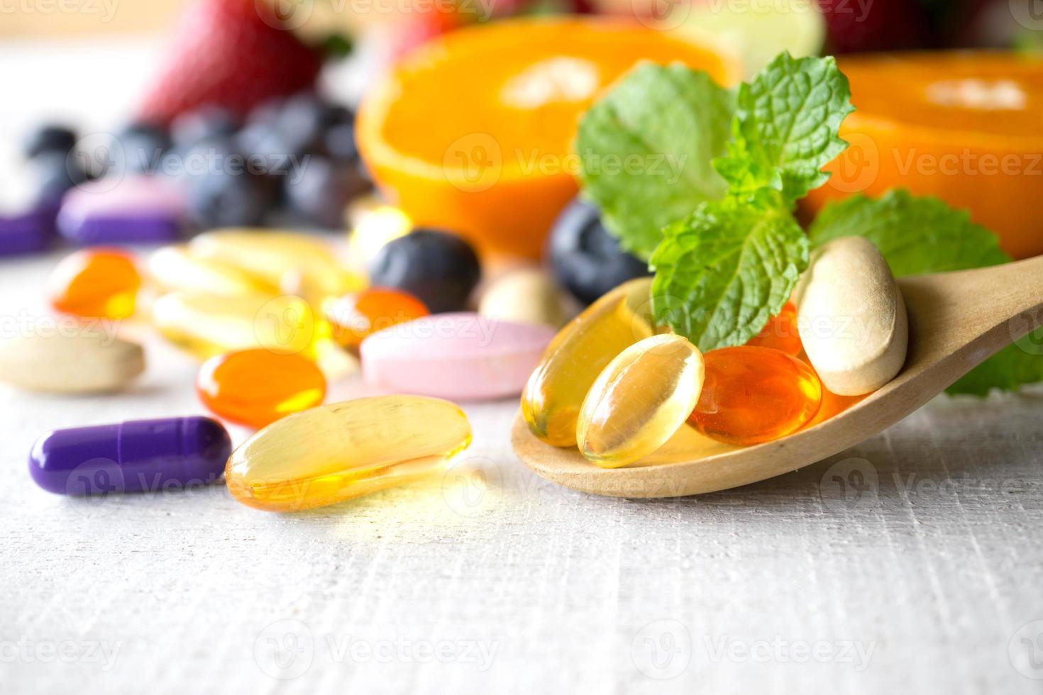 färgglada piller och kapslar i träsked med färsk frukt. vitaminer och tillägg från frukt koncept. foto