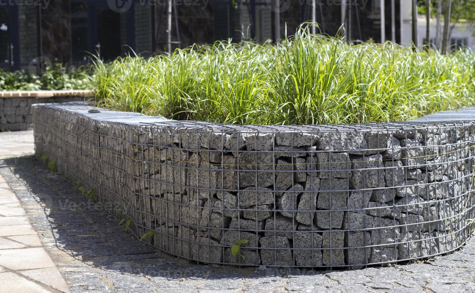 korg Stöd vägg tillverkad av granit gabion. gabioner i de trädgård. modern gabion staket med stenar i tråd maska. gabion tråd maska fäktning med naturlig sten och buskar. foto