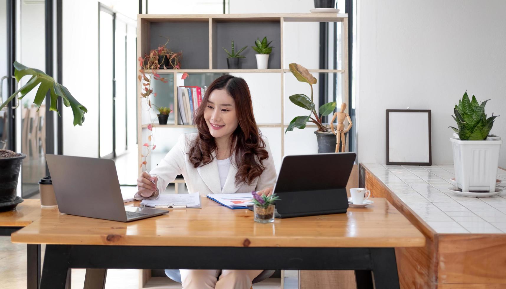 vacker ung asiatisk kvinna sitter på kafé med bärbar dator. glad ung affärskvinna sitter vid bordet i café med tab top dator. foto