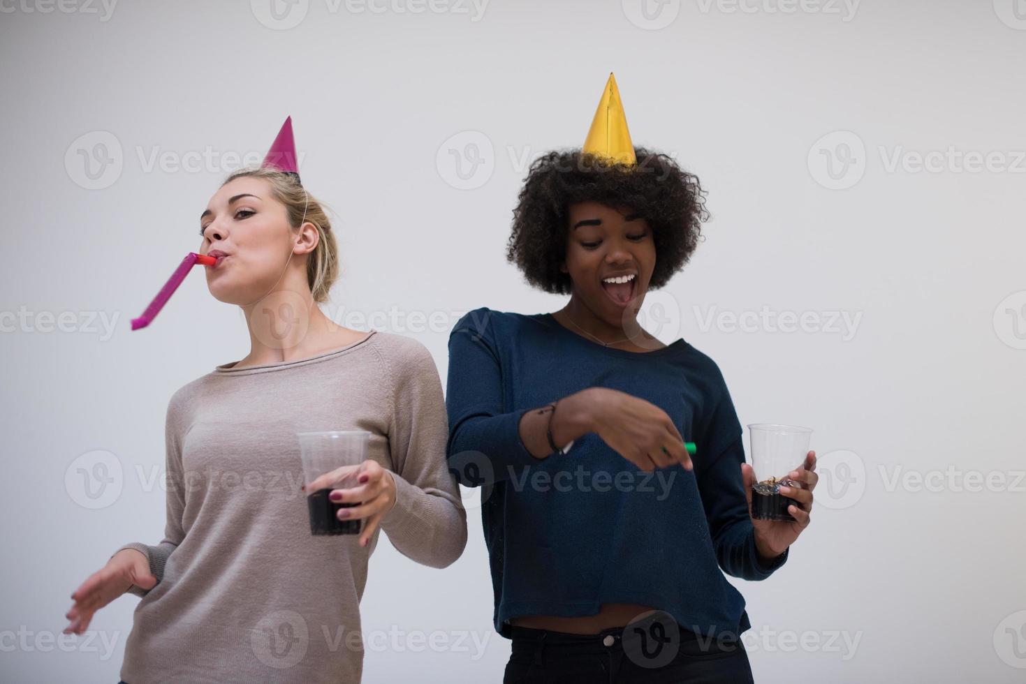 leende kvinnor i fest caps blåser till visselpipor foto