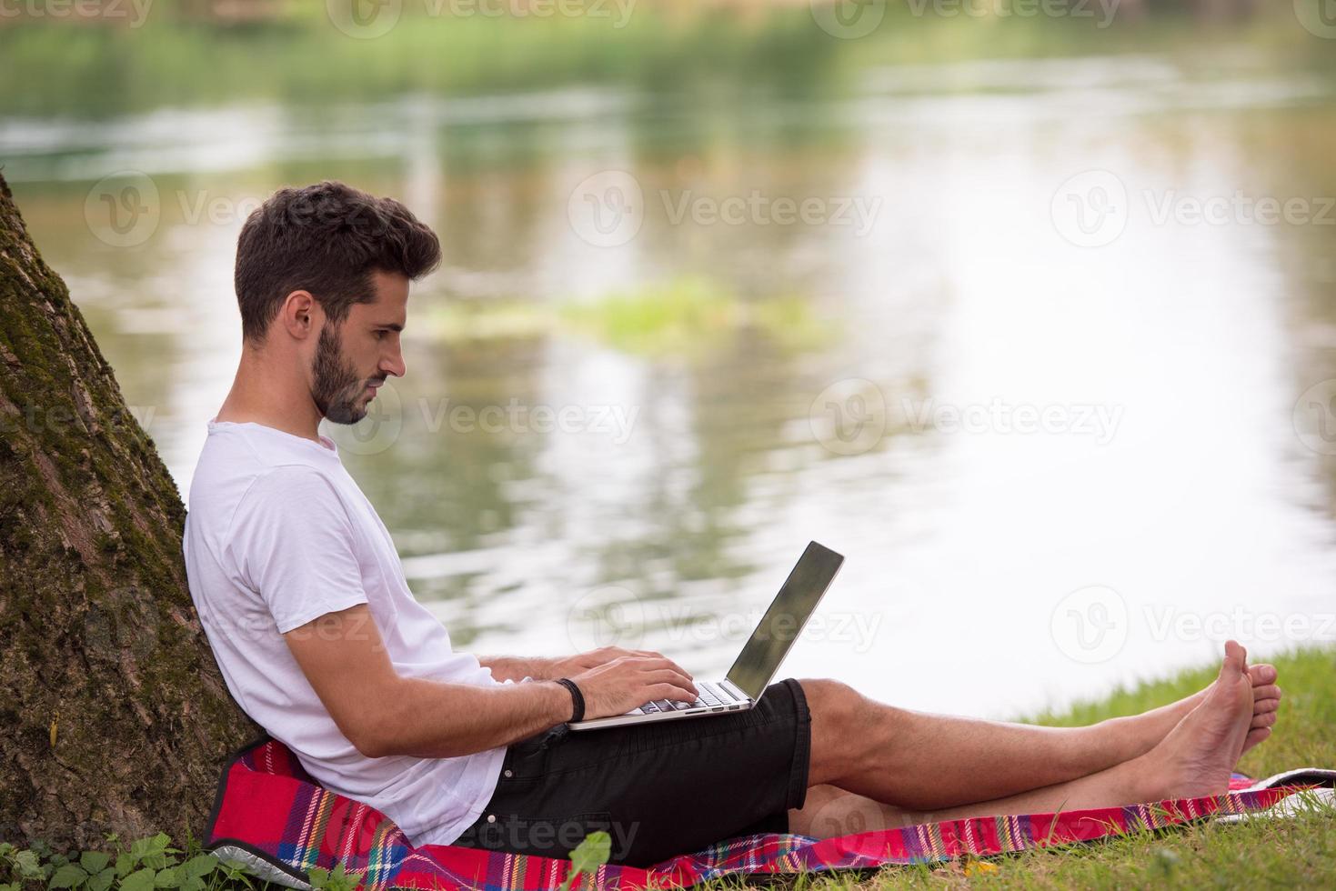 man använder en bärbar dator på stranden av floden foto