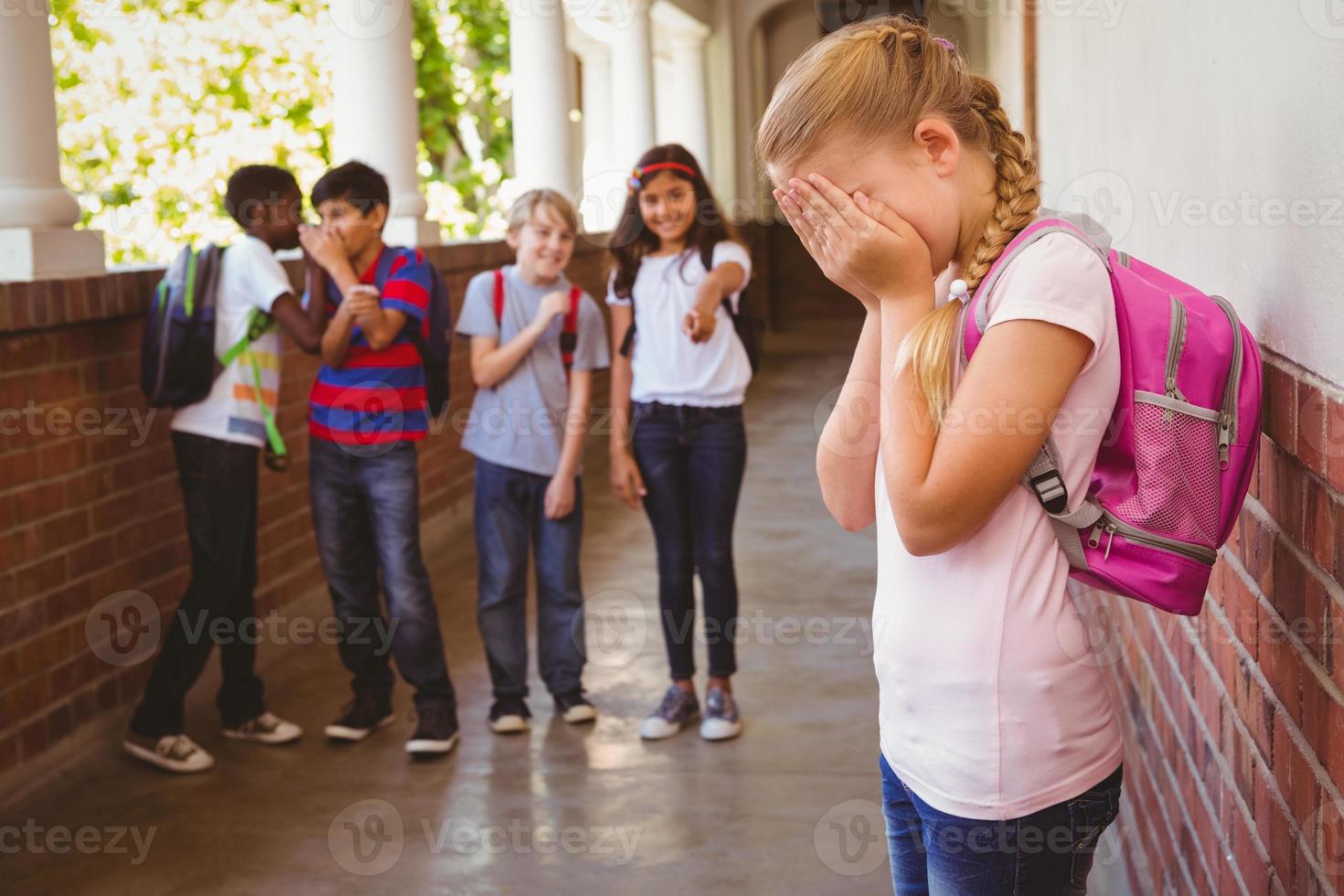 ledsen skolflicka med vänner i bakgrunden på skolakorridoren foto