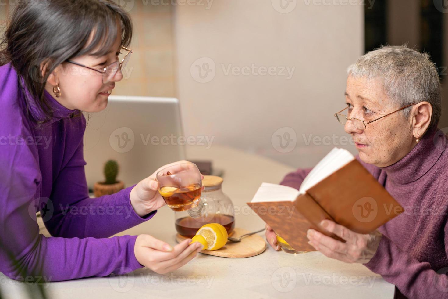mormor och barnbarn dricker te när de sitter vid bordet och läser en bok. foto