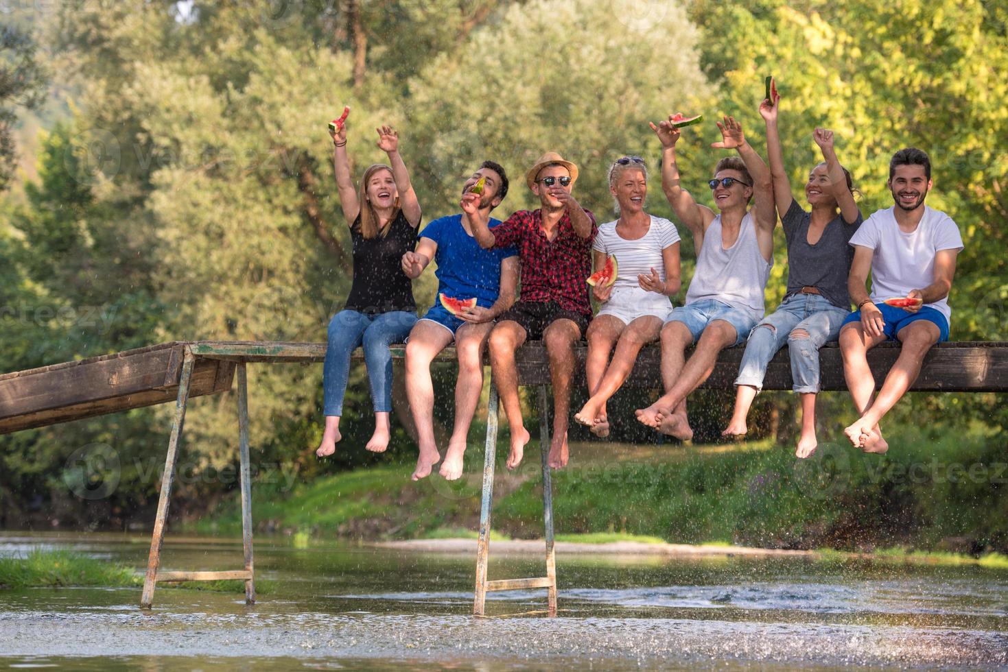 vänner njuter vattenmelon medan Sammanträde på de trä- bro foto