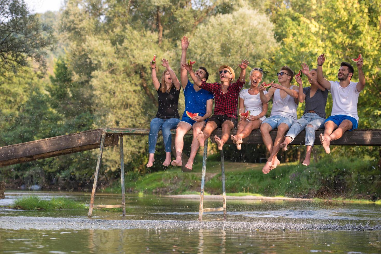 vänner njuter vattenmelon medan Sammanträde på de trä- bro foto