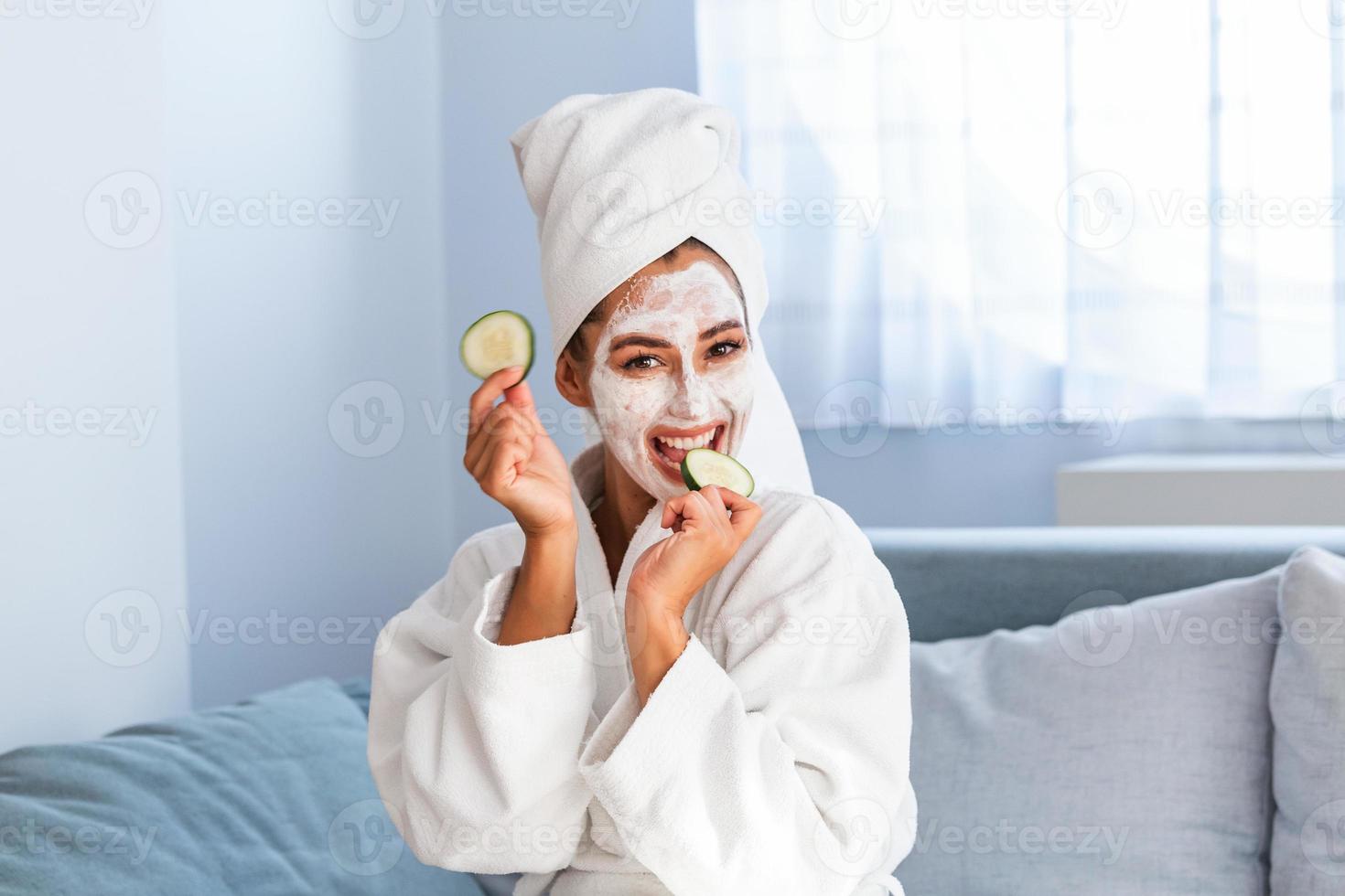 skön ung kvinna med ansiktsbehandling mask på henne ansikte innehav skivor av färsk gurka. hud vård och behandling, spa, naturlig skönhet och kosmetologi begrepp. foto