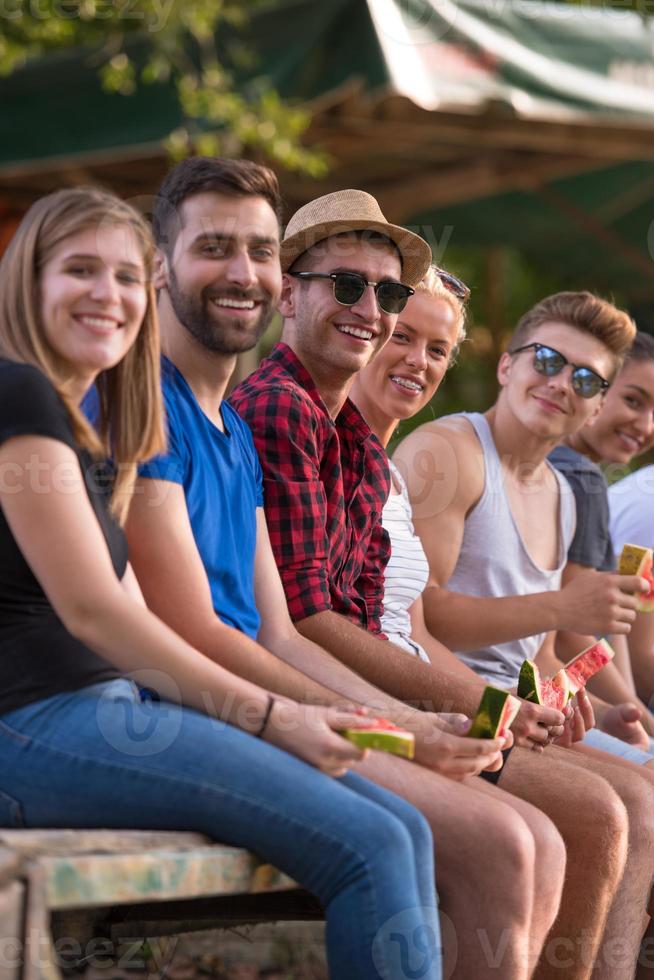 vänner njuter vattenmelon medan Sammanträde på de trä- bro foto