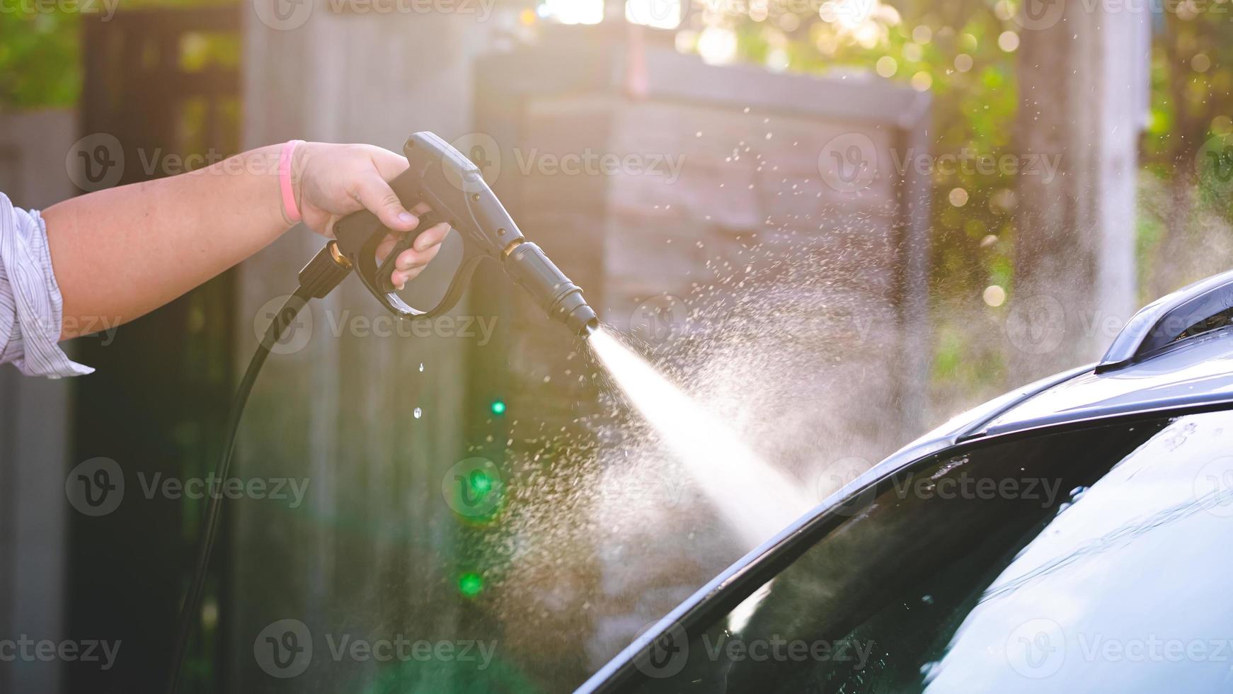 mannens hand innehav en svart högt tryck munstycke, rengöring de bil. vatten droppar spridd. solljus i de kväll. foto