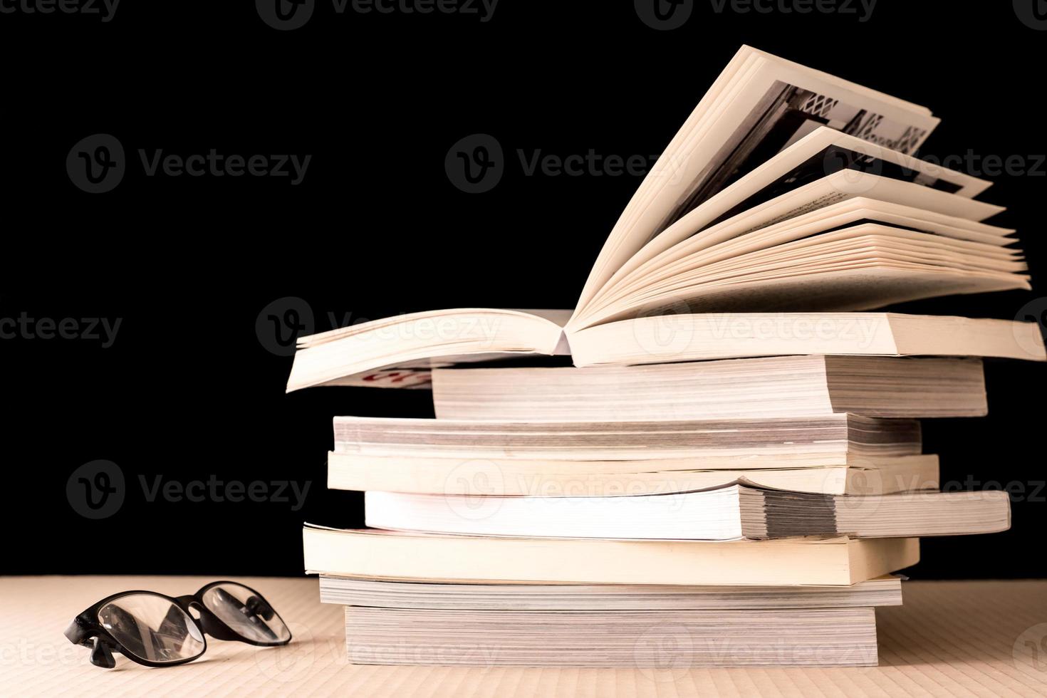 stack av böcker och glasögon på trä- tabell, svart bakgrund foto