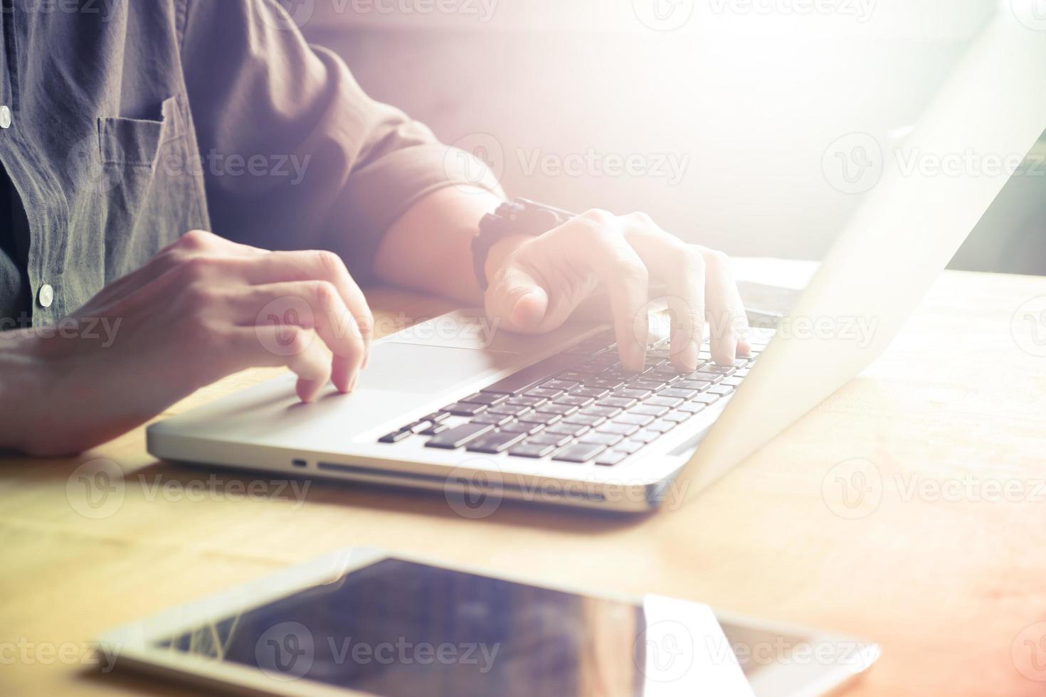 stänga upp av manlig händer använder sig av bärbar dator på de tabell, tonad med solljus foto